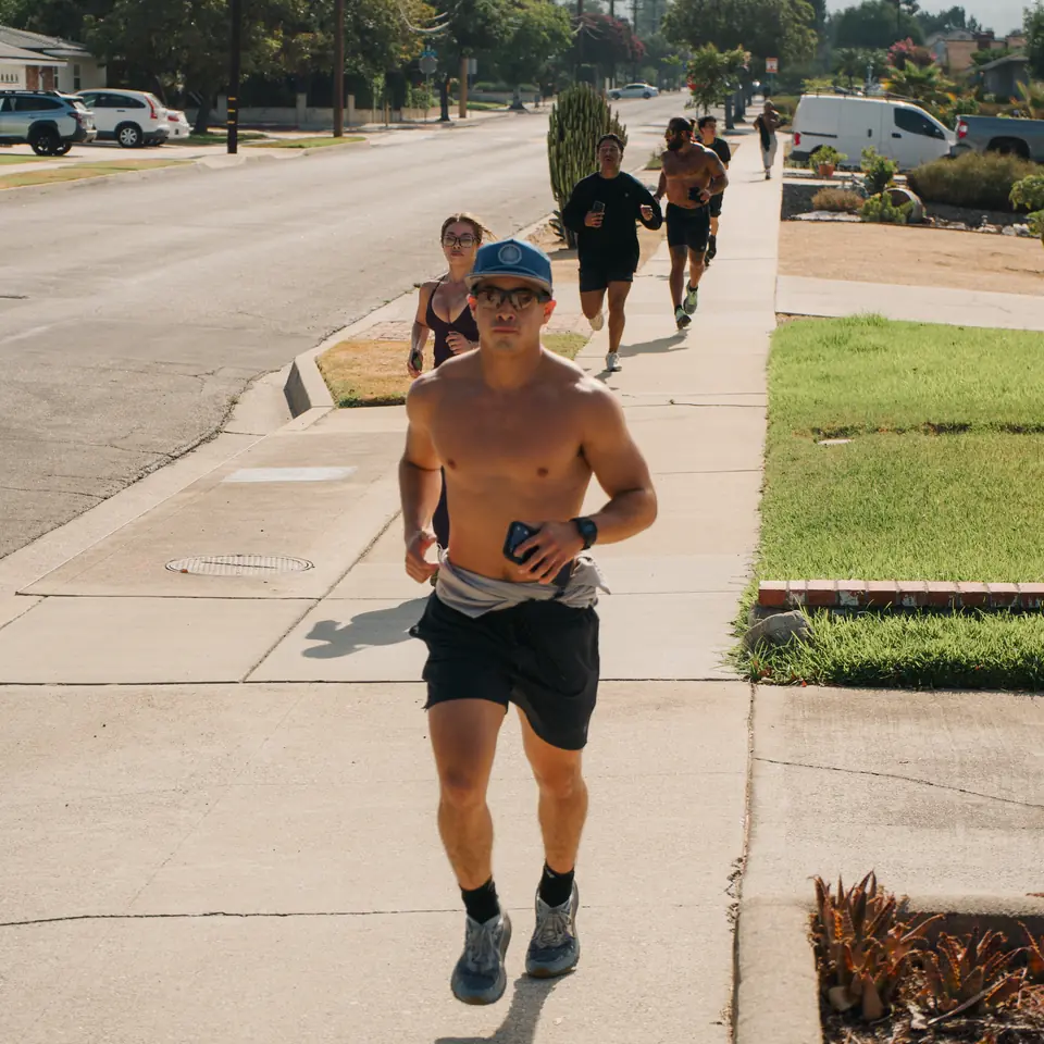 Shirtless runner with a phone leading a small group up the sidewalk