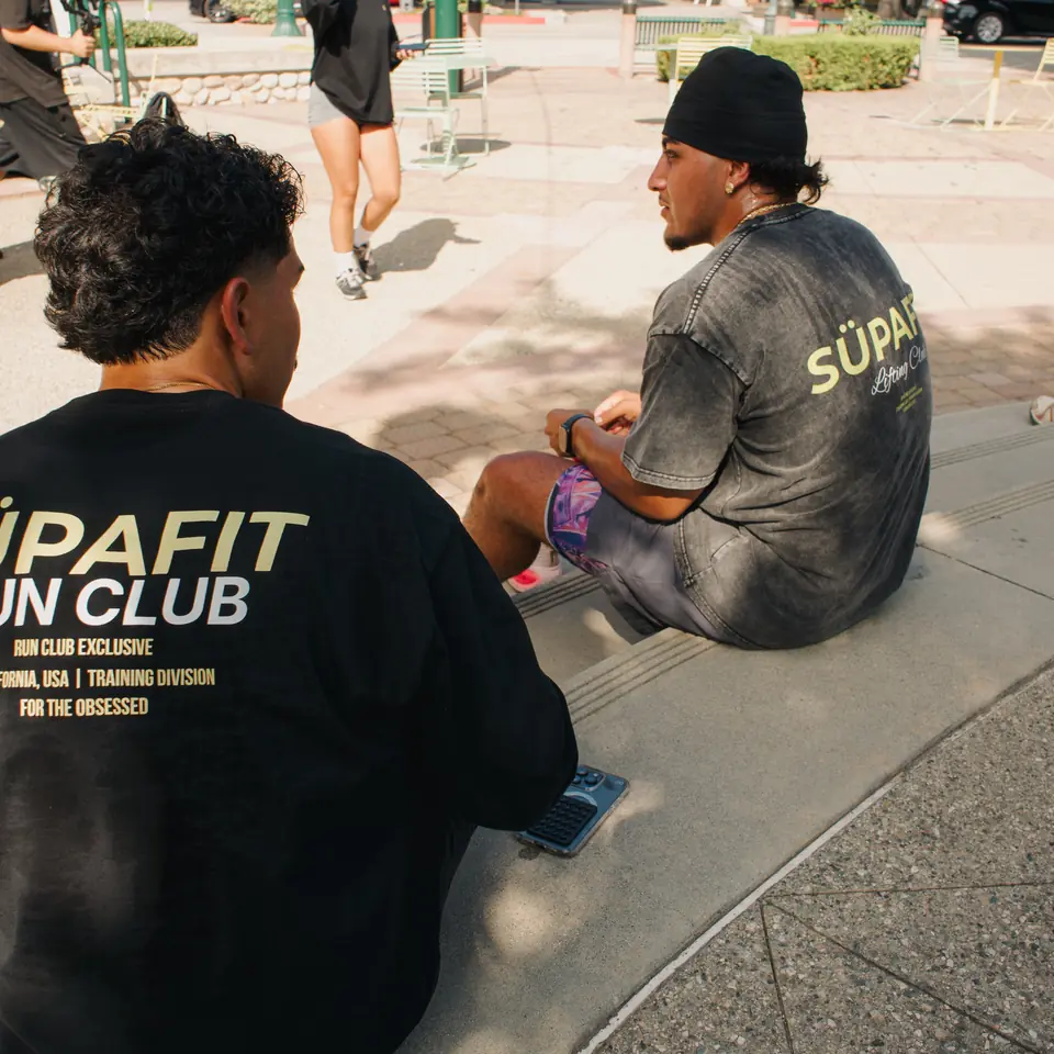 Two runners in SÜPAFIT shirts sitting on the plaza steps catching their breath