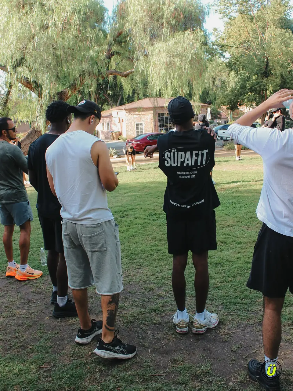 Runner in a SÜPAFIT Athletic Club tee hanging out with friends under a willow tree