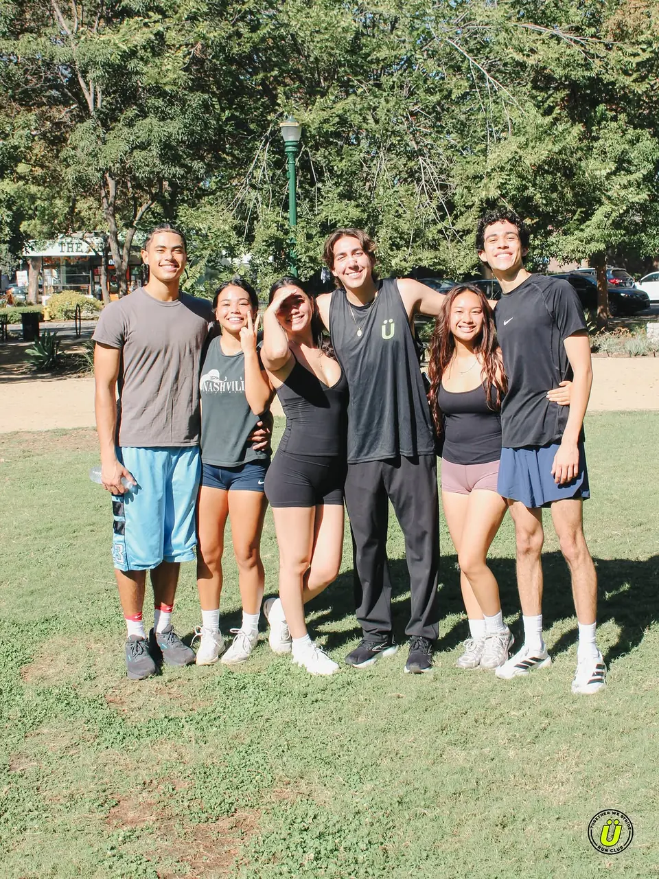 Six friends smiling and posing together on the grass after the run