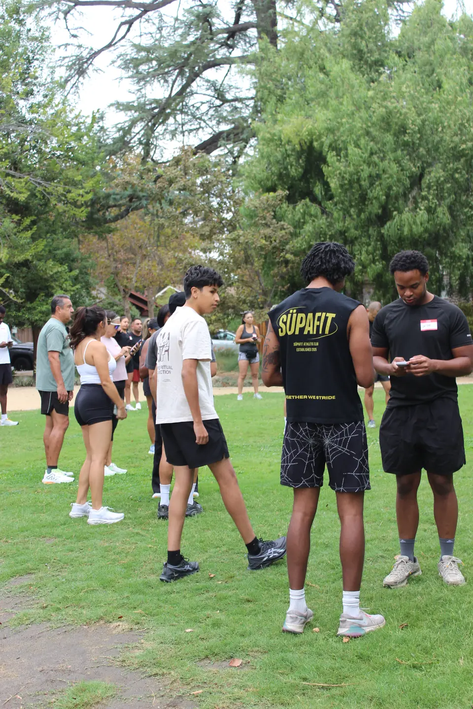 Two runners comparing phones on the grass while new faces meet nearby