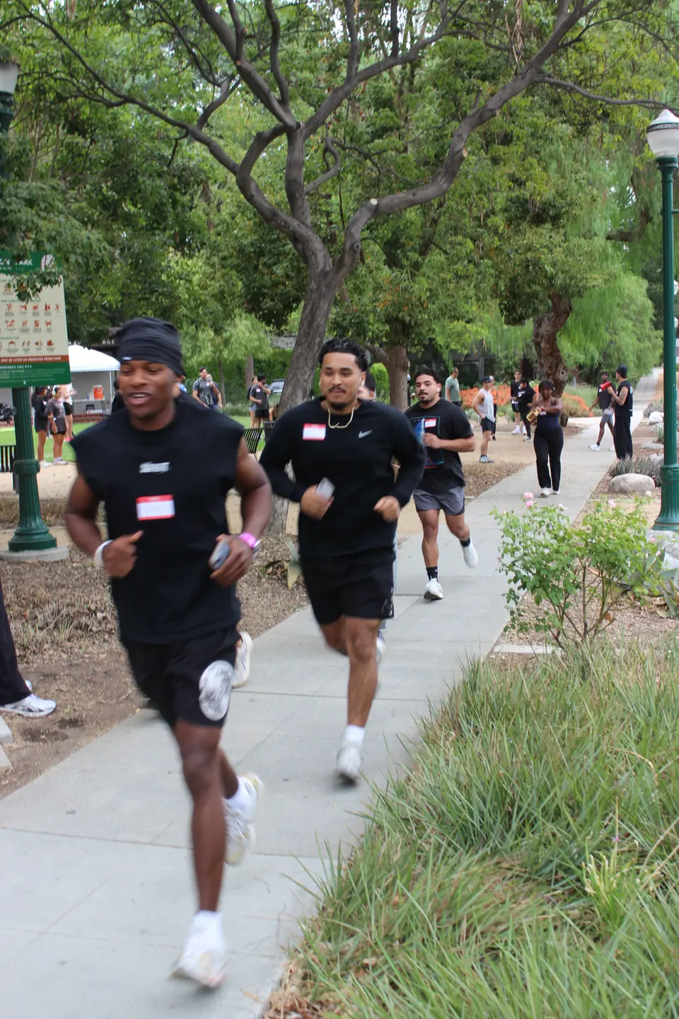 Runners in black tees picking up the pace on a park path lined with grass